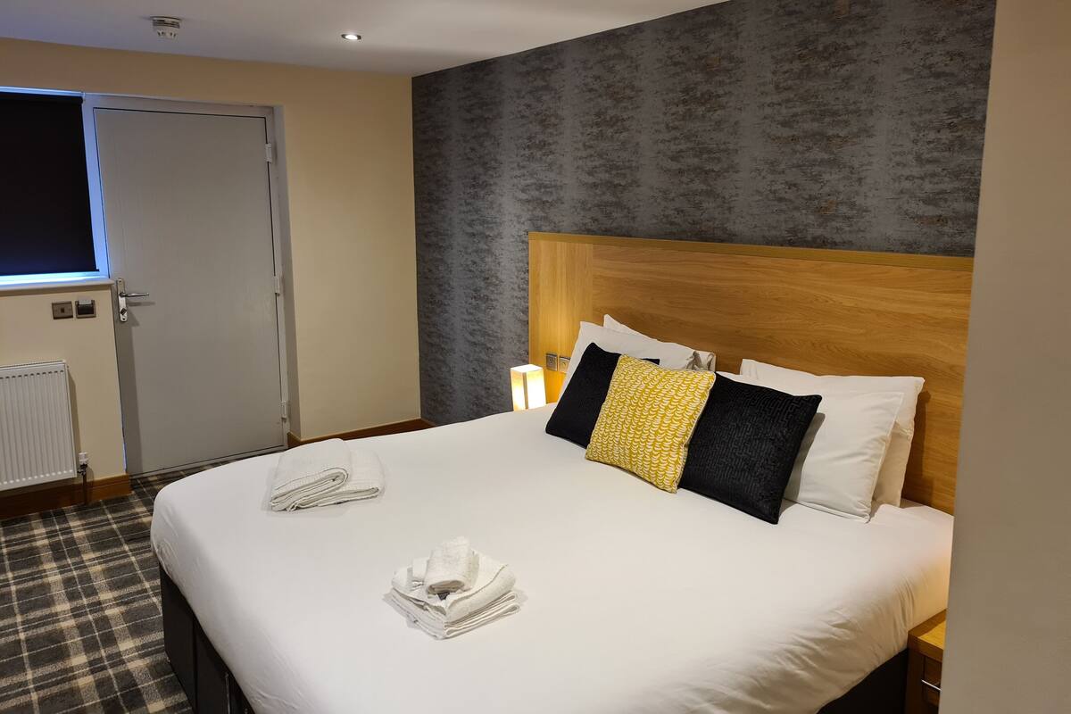 A hotel room with a large bed, a wooden headboard, and a plaid-patterned floor.