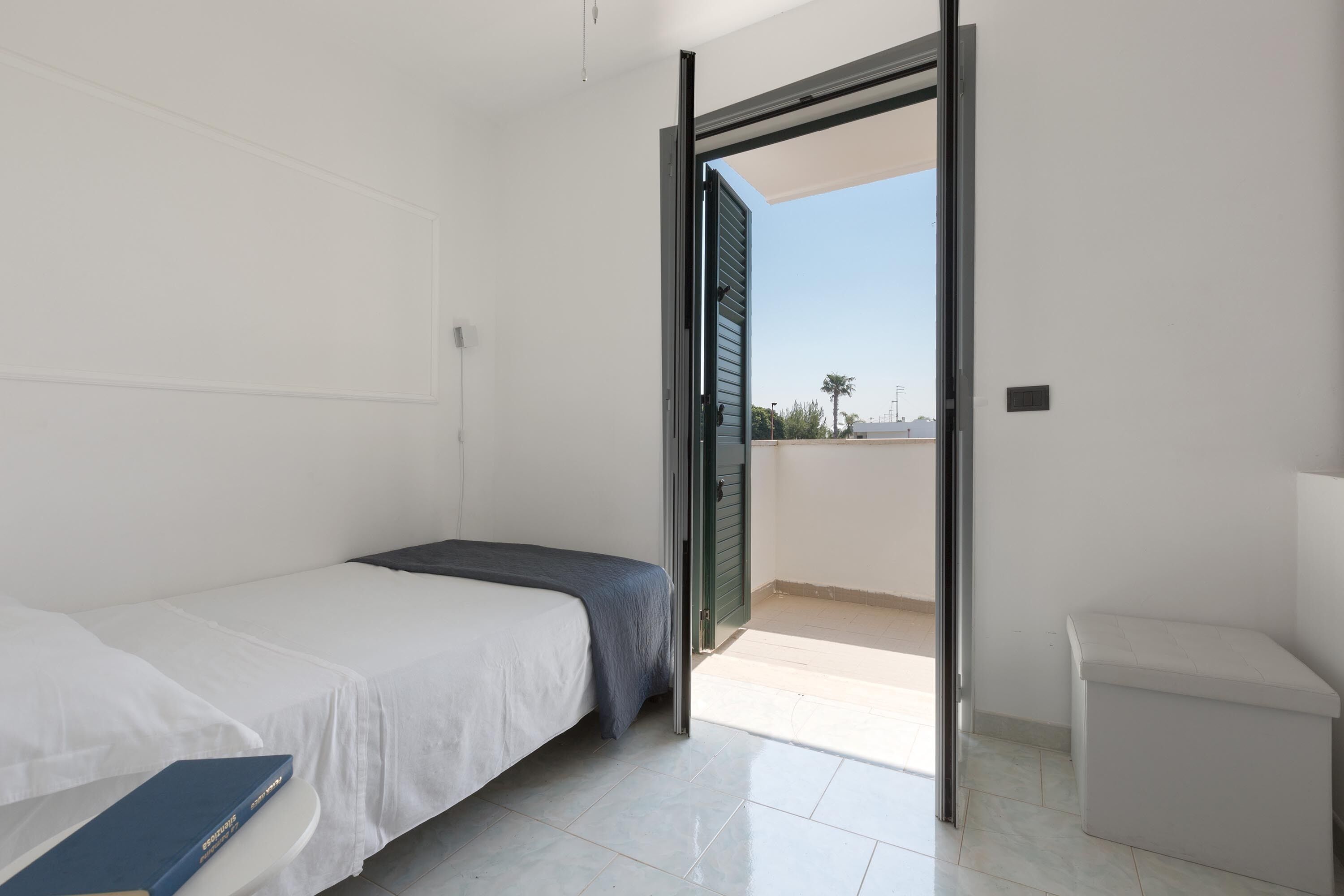 A bedroom with a bed, a small bedside table, and an open door leading to a balcony.