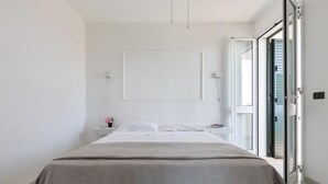 A modern bedroom with a bed, a bedside table, and a view through an open door. - 3542 Villa Beach by Barbarhouse (Melendugno)