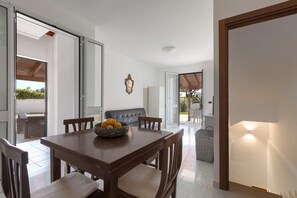 A dining area with a wooden table, chairs, and a bowl of fruit. There is a sliding glass door leading to an outdoor seating area.