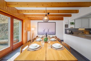 Comedor con una mesa de madera para seis comensales, un ventanal grande y una cocina visible a la derecha.