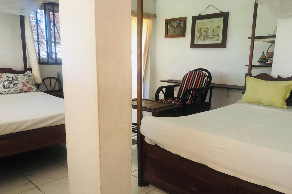 A hotel room with two beds, a chair, a table, and a window with curtains.