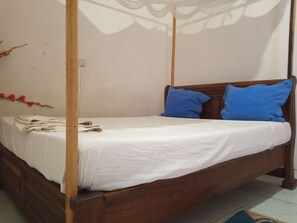 Una cama con dosel cubierta con ropa de cama blanca y almohadas azules, cabecero de madera y pared blanca con decoración floral.