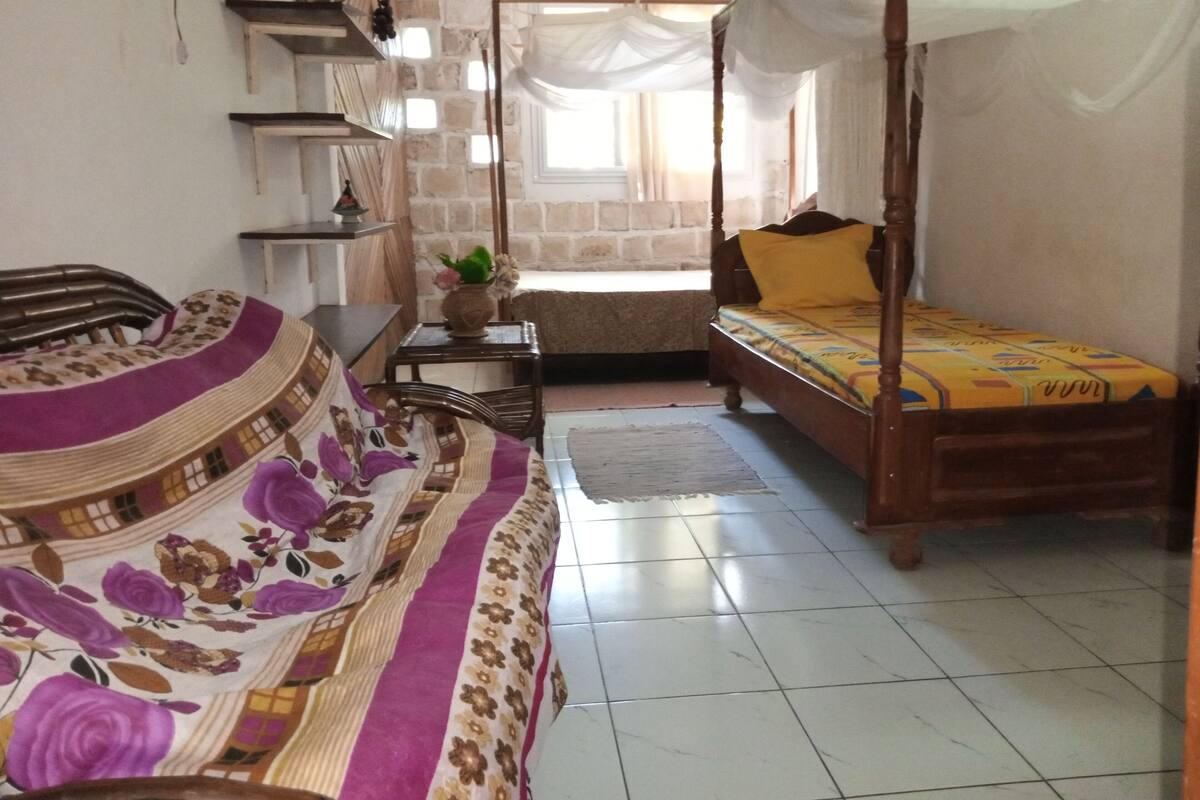 A room with a bed, a sofa, a small table, and a window.
