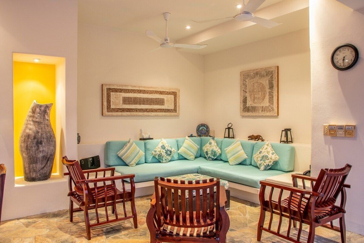 A living room with a light blue sofa, wooden chairs, a large vase, and framed artwork on the walls.