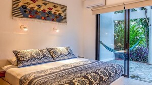 A bedroom with a patterned bedspread, a decorative wall hanging, and a view of a lush garden through a sliding glass door. - Villa Vista Hermosa Huatulco (Santa María Huatulco)