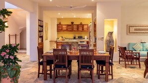 A spacious dining area with a large wooden table and chairs, a kitchen in the background, and a cozy seating area with cushions. - Villa Vista Hermosa Huatulco (Santa María Huatulco)