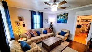 Un salon comprenant un ensemble de canapés, une table basse, un ventilateur de plafond et un tableau accroché au mur.