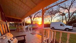 Une véranda couverte avec un barbecue, une terrasse en bois et une vue sur le coucher du soleil et les voitures garées.