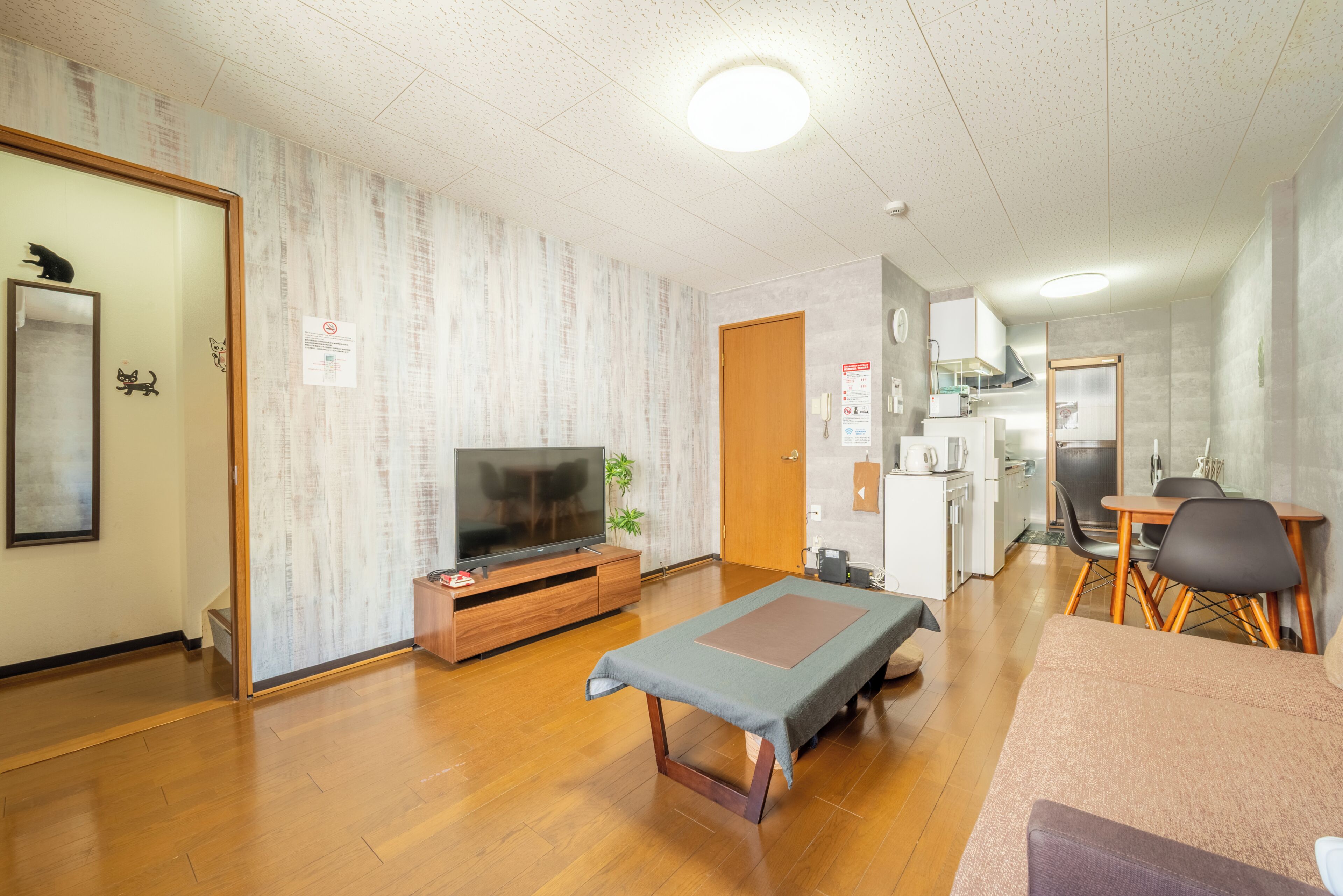 A living room with a television, a sofa, a small table, and a kitchenette in the background.