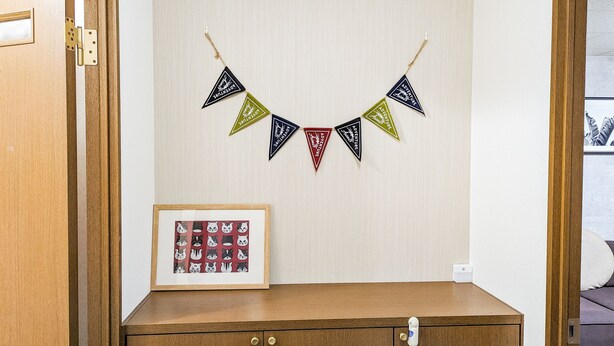 A wooden dresser with a framed picture of cats. Above the dresser, there is a wall with a string of triangular flags in black, red, and green colors.