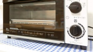 A compact toaster oven with a digital display and control knobs, placed on a checkered tablecloth. - DoumoTengachaya (Osaka)