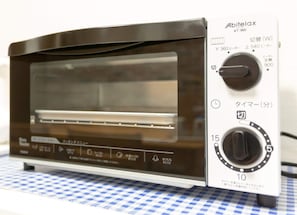 A compact toaster oven with a digital display and control knobs, placed on a checkered tablecloth. - DoumoTengachaya (Osaka)