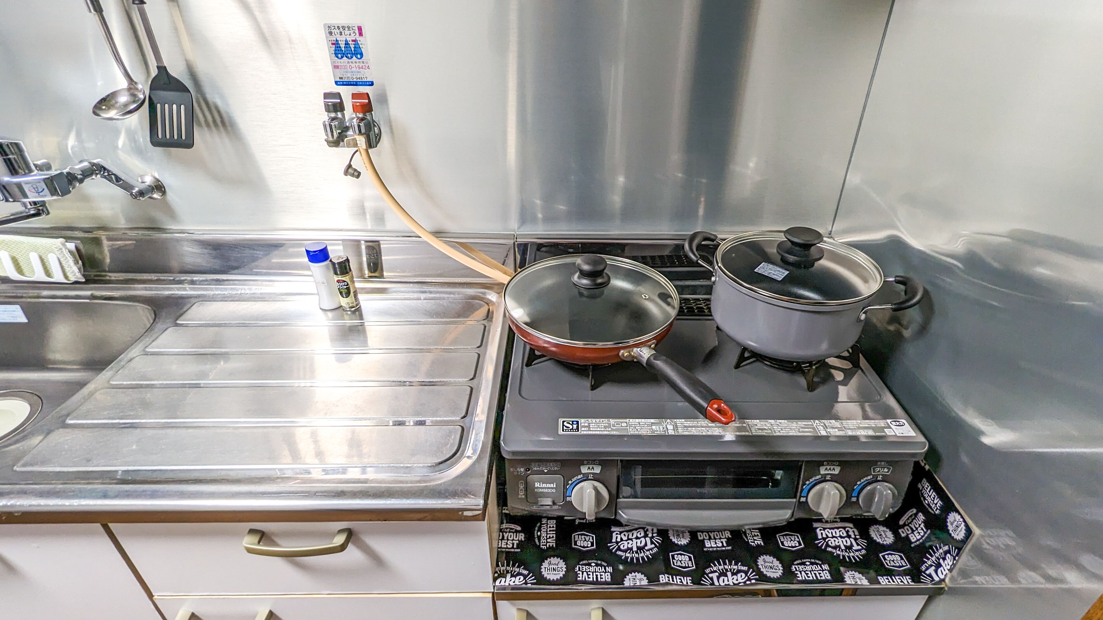 A kitchen with stainless steel appliances, including a stove with pots and a pan, a sink, and a faucet.