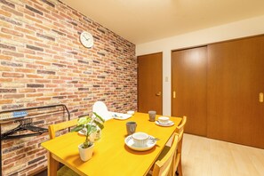 A dining area with a brick wall, a clock, wooden doors, and a yellow table with chairs. - DoumoTengachaya (Osaka)