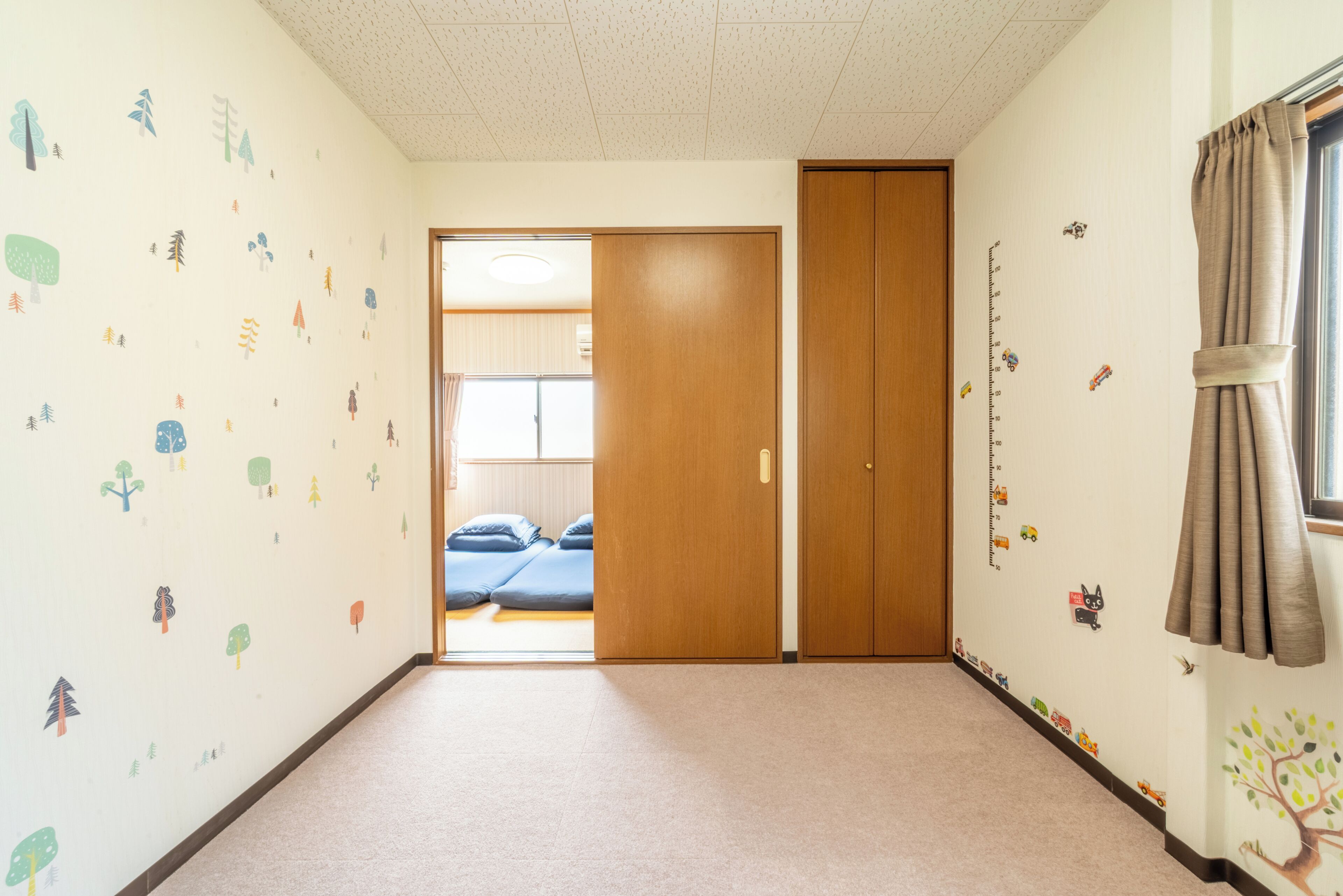 A room with a carpeted floor, a wooden door, and a window with curtains.