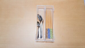 A clear plastic container with utensils and chopsticks on a wooden surface. - DoumoTengachaya (Osaka)