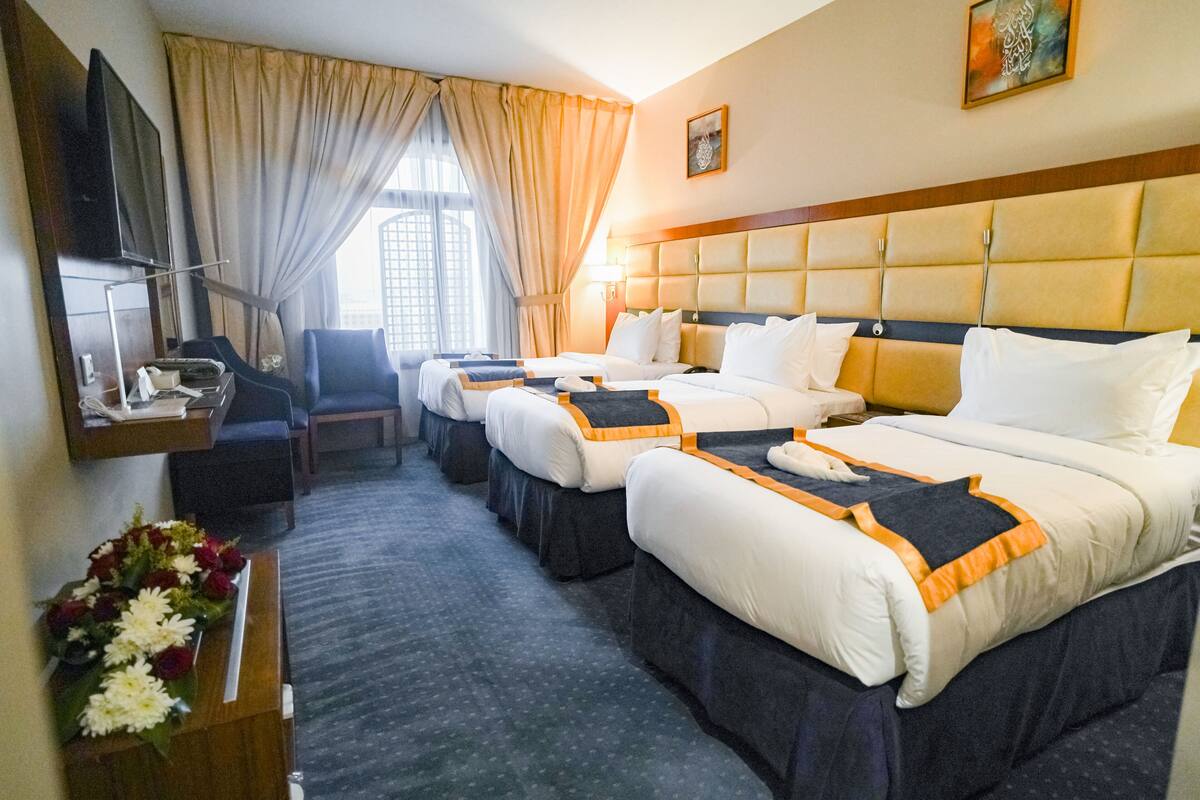 A hotel room with three beds, a desk with a telephone, a chair, a TV, and a window with curtains.