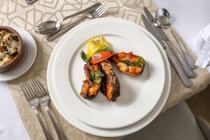 Un plato de pollo a la parrilla con vegetales y limón sobre una mesa con cubiertos.