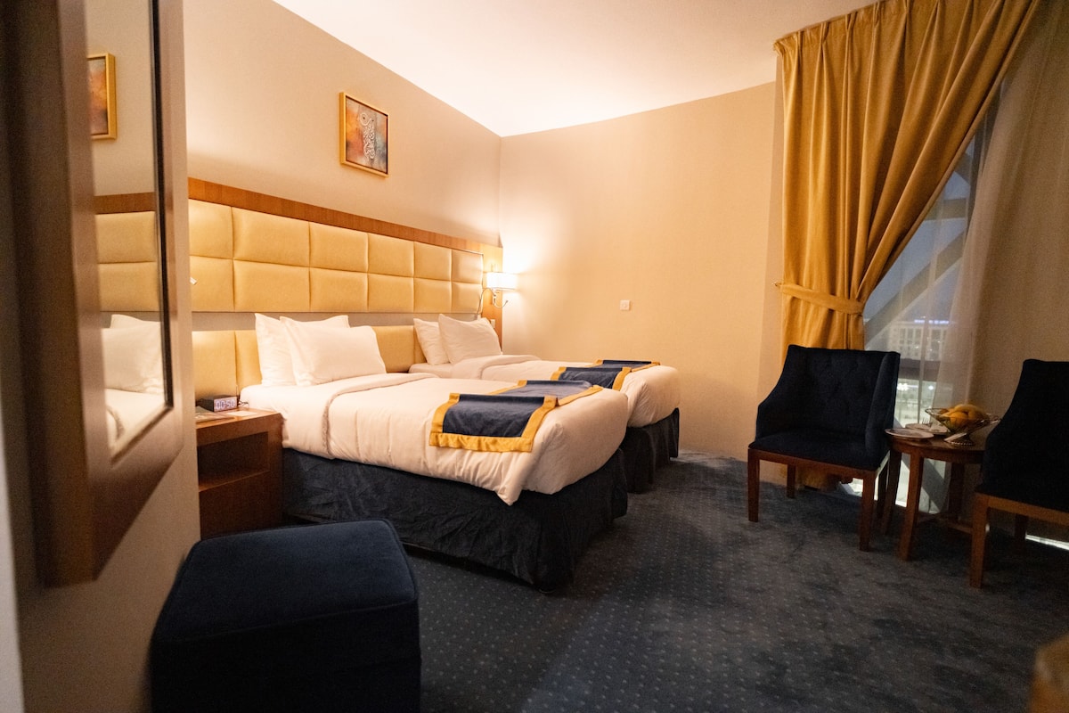 A hotel room with a large bed, two bedside tables, a chair, a small table, and a window with curtains.
