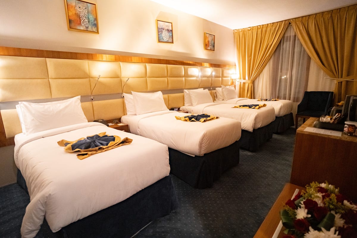 A hotel room with four beds arranged in a row, a wooden headboard, and a desk with a lamp.