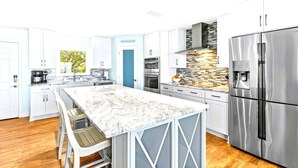Una cucina moderna con mobili bianchi, un piano di lavoro in marmo, elettrodomestici in acciaio inossidabile e forno integrato.