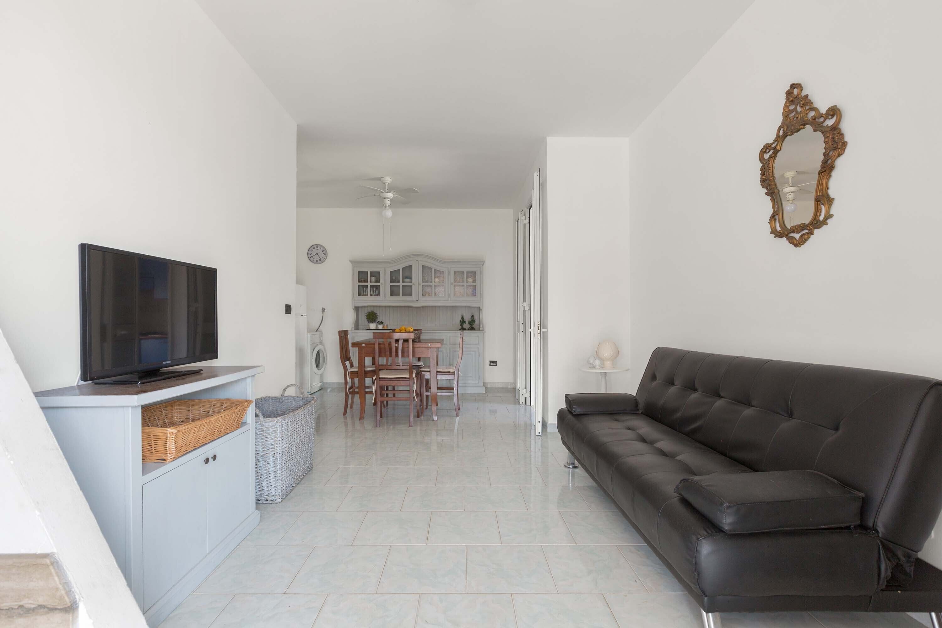 A living room with a TV, sofa, and a dining area with chairs and a table.