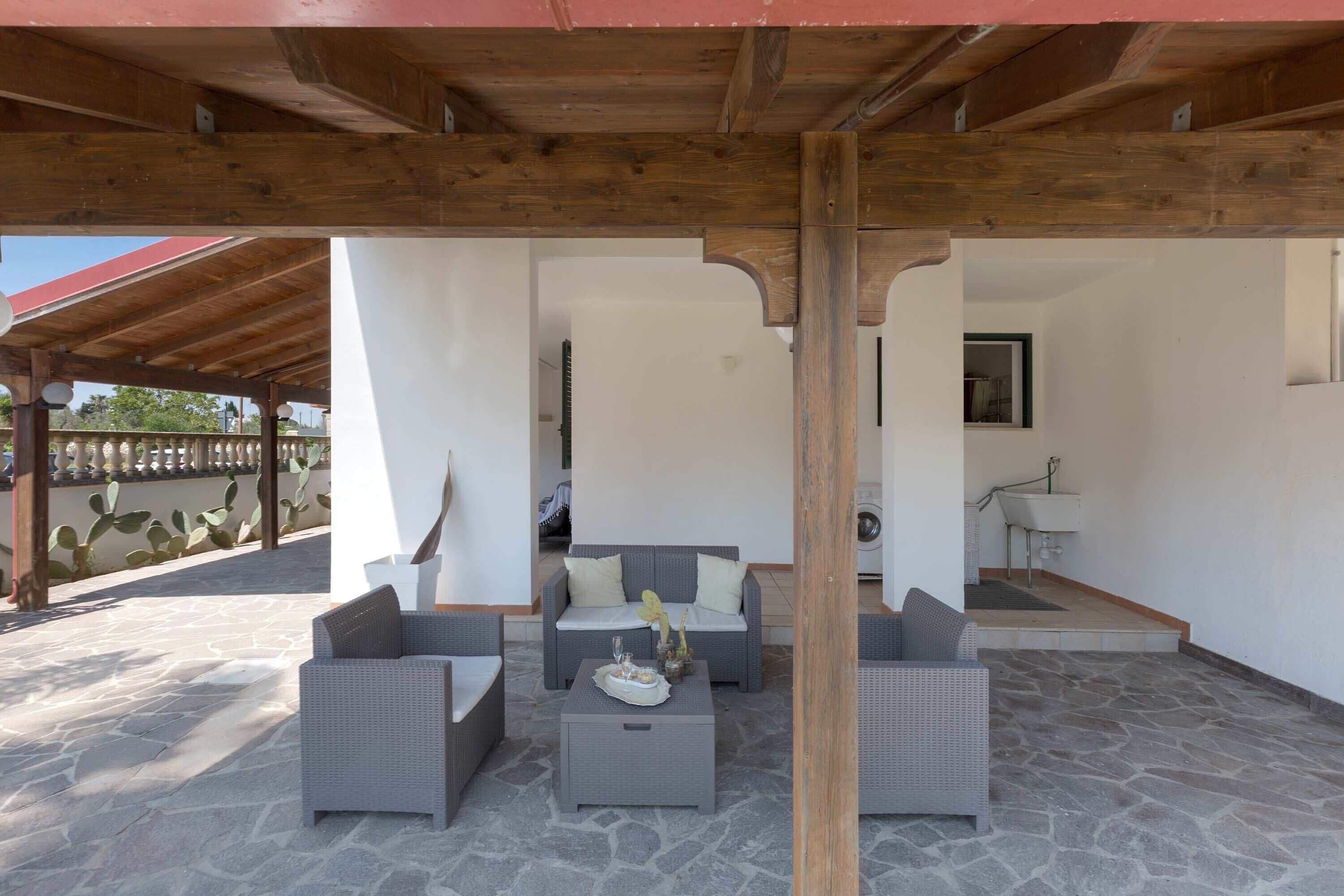 A covered outdoor seating area with wicker furniture and a stone floor.