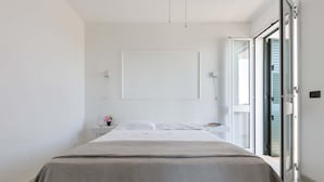 Un dormitorio minimalista con cama, mesita de noche y vista a través de un umbral abierto.