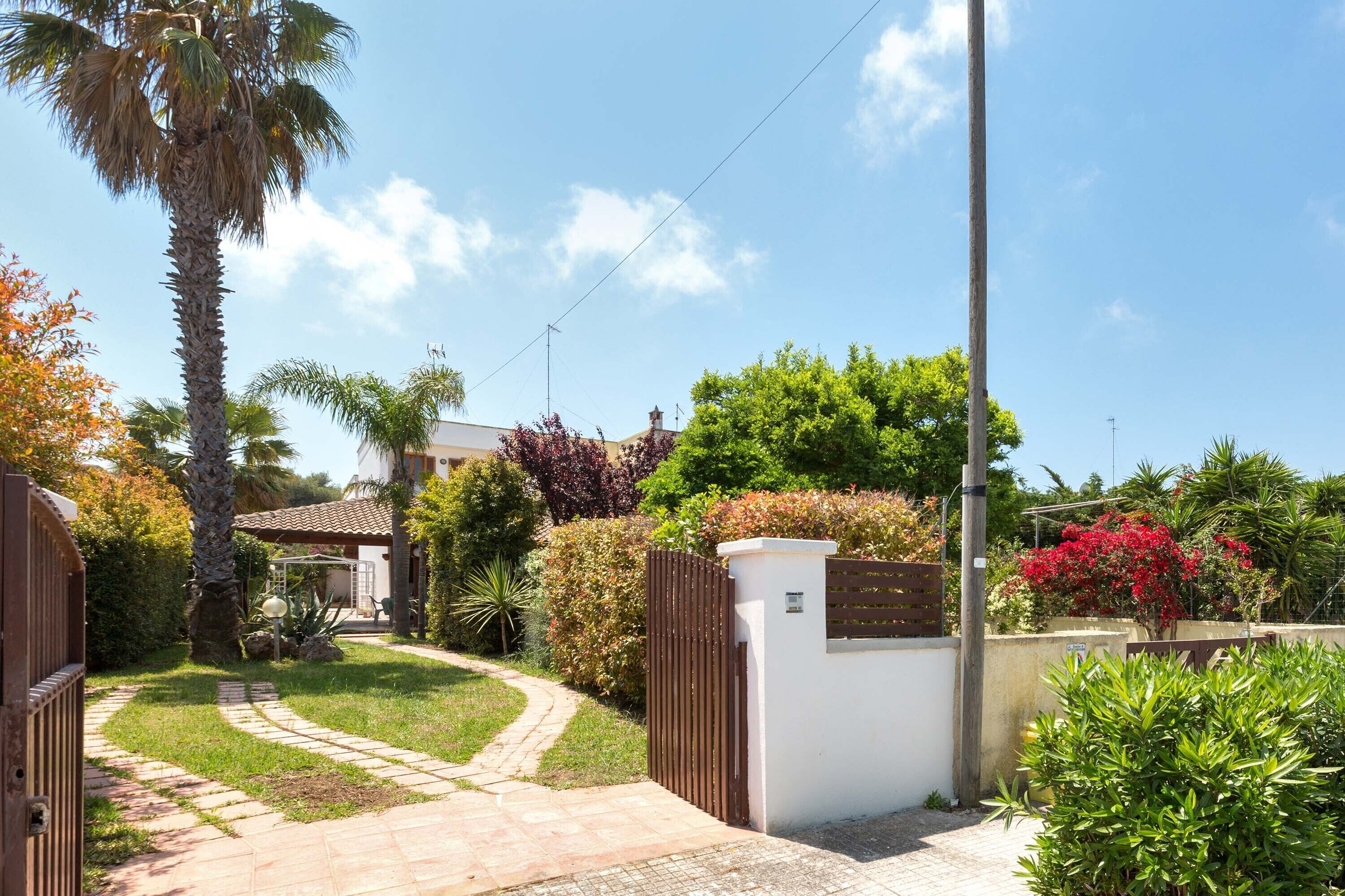 A gated residential area with a paved pathway leading to a house with a tiled roof.