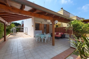 A covered patio area with a dining table and chairs, a wooden pergola, and a fenced garden. - 3476 Villa Zen Garden by Barbarhouse (Melendugno)