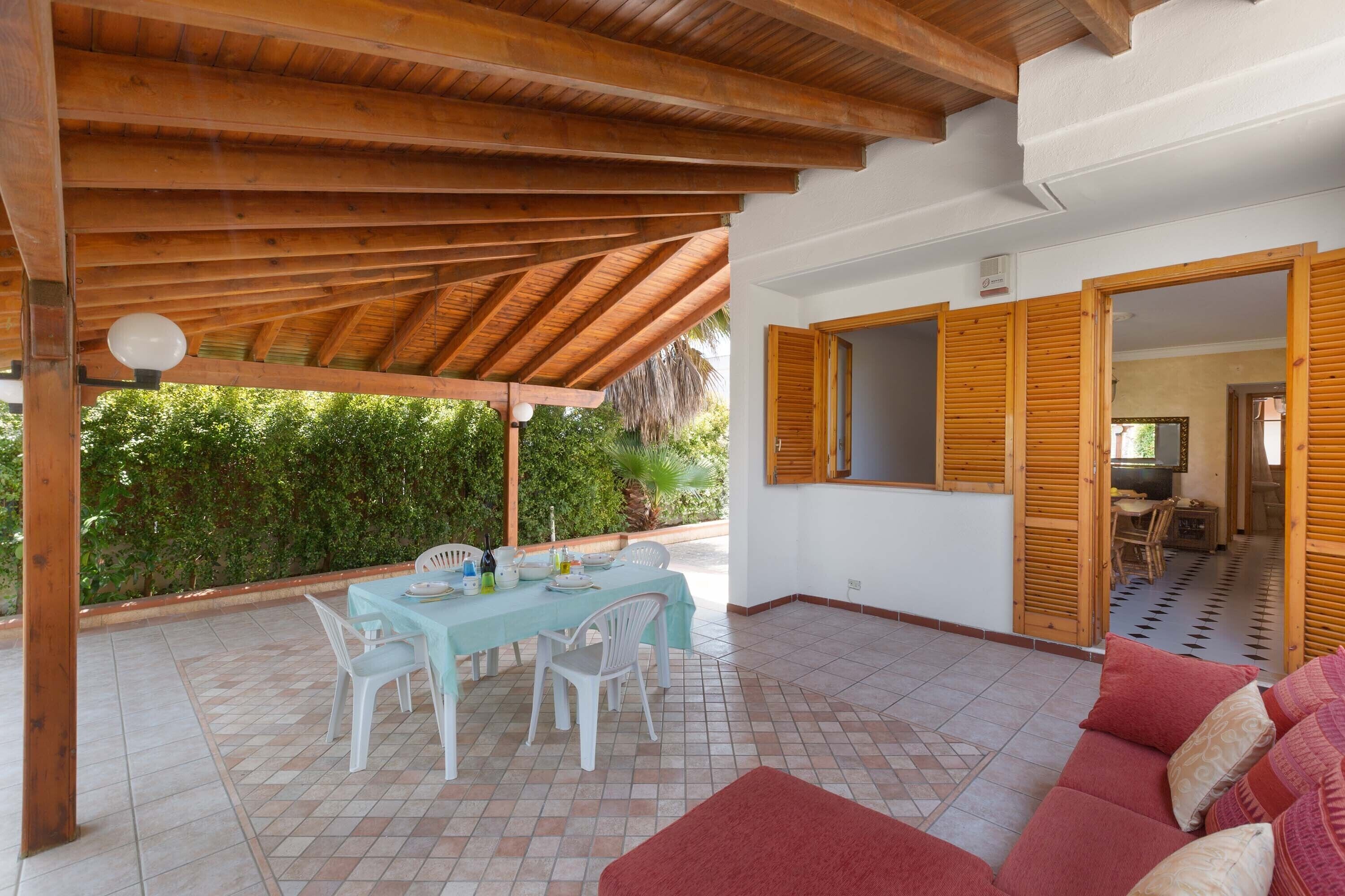 A covered patio area with a wooden ceiling, a dining table with chairs, and a red sofa.