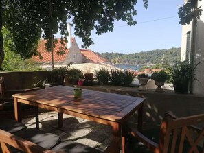 Eine Terrasse im Freien mit einem Holztisch und Stühlen, umgeben von Kübelpflanzen.