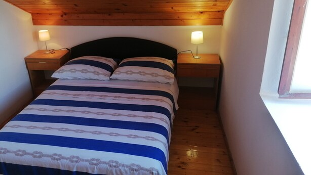 A narrow room with a bed, two bedside tables with lamps, wooden ceiling, and a window. - Cozy Seafront Retreat in Cavtat (Konavle)