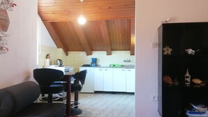 A kitchen with white cabinets, a black countertop, and a wooden ceiling. There is a dining area with a black chair and a table. - Cozy Seafront Retreat in Cavtat (Konavle)