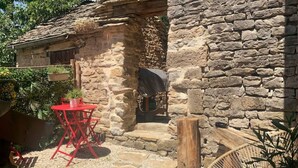 A stone building with a rustic exterior, a red folding table, and a wooden chair outside. - Maison Chaleureuse Avec SPA (Savigny-sous-Mâlain)