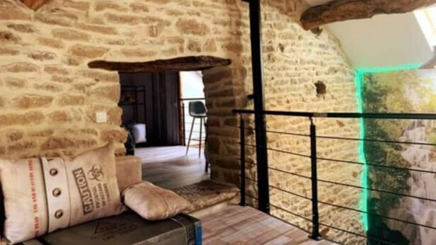A rustic stone interior with a wooden ceiling, a metal railing, and a view of a room with a chair and a table. - Maison Chaleureuse Avec SPA (Savigny-sous-Mâlain)