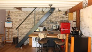 A rustic kitchen with a wooden island, bar stools, a red refrigerator, and a stone wall. - Maison Chaleureuse Avec SPA (Savigny-sous-Mâlain)