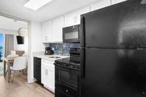 Una cocina moderna con armarios blancos, un refrigerador negro, una estufa y un microondas.