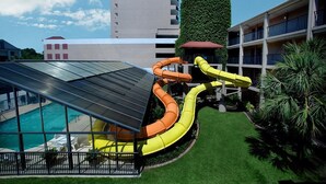 Un espace piscine aménagé sur le toit, doté d’un toboggan, entouré d’une pelouse bien entretenue et d’un bâtiment avec des balcons.