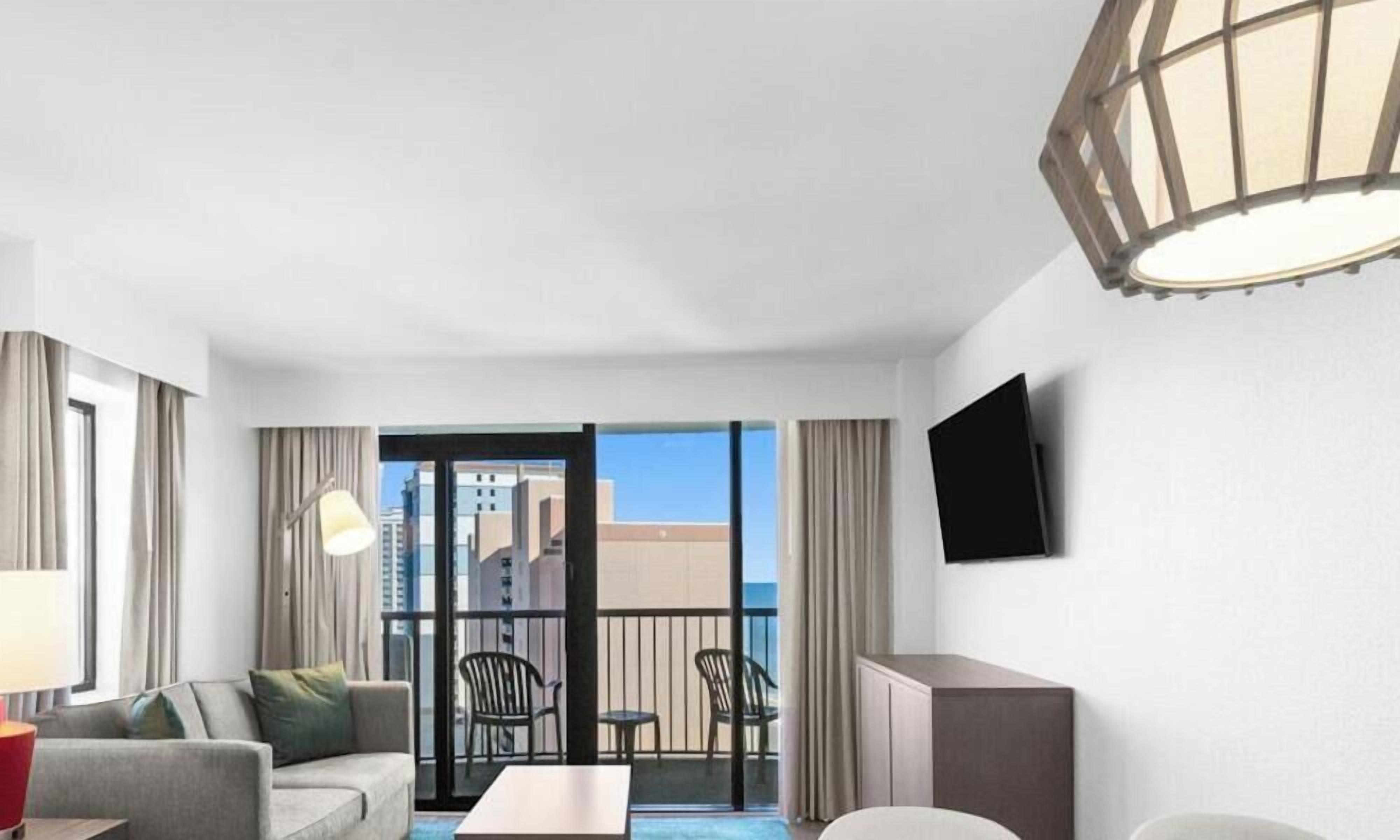 Ein Hotelzimmer mit Balkon, einer Couch, einem Tisch und einem Fernseher.