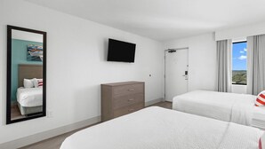 Une chambre d’hôtel avec deux lits, un téléviseur à écran plat, une commode et une porte donnant sur un balcon avec vue.