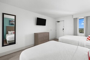 A hotel room with two beds, a flat-screen TV, a dresser, and a door leading to a balcony with a view.