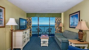 Une chambre avec un balcon, une télévision, un canapé, une petite table et une lampe.