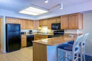 A kitchen with wooden cabinets, a black refrigerator, a microwave, and a granite countertop.
