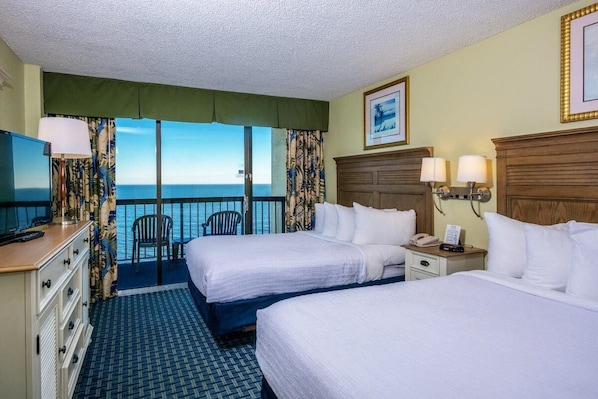 Quarto de hotel com duas camas, uma escrivaninha com telefone, uma cadeira, televisão e vista para o oceano.