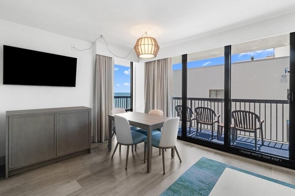 Une chambre moderne  équipée d’une table à manger, de chaises, d’un téléviseur fixé au mur et d’un balcon avec des meubles d’extérieur.