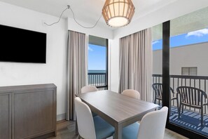 Quarto moderno com mesa de jantar de madeira, quatro cadeiras, televisão na parede e varanda com mobiliário exterior.