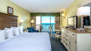 A hotel room with a large bed, a desk with a chair, a television, and a view of the ocean.