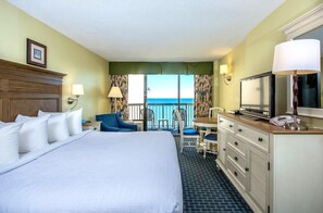 A hotel room with a large bed, a desk with a chair, a television, and a view of the ocean.